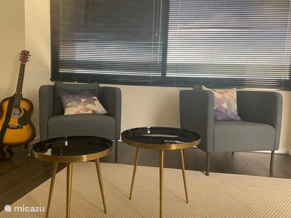 Dos sofás individuales y modernas mesas de café redondas forman un rincón acogedor con vista al campo de golf a través de la ventana. El estilo se encuentra con la relajación.