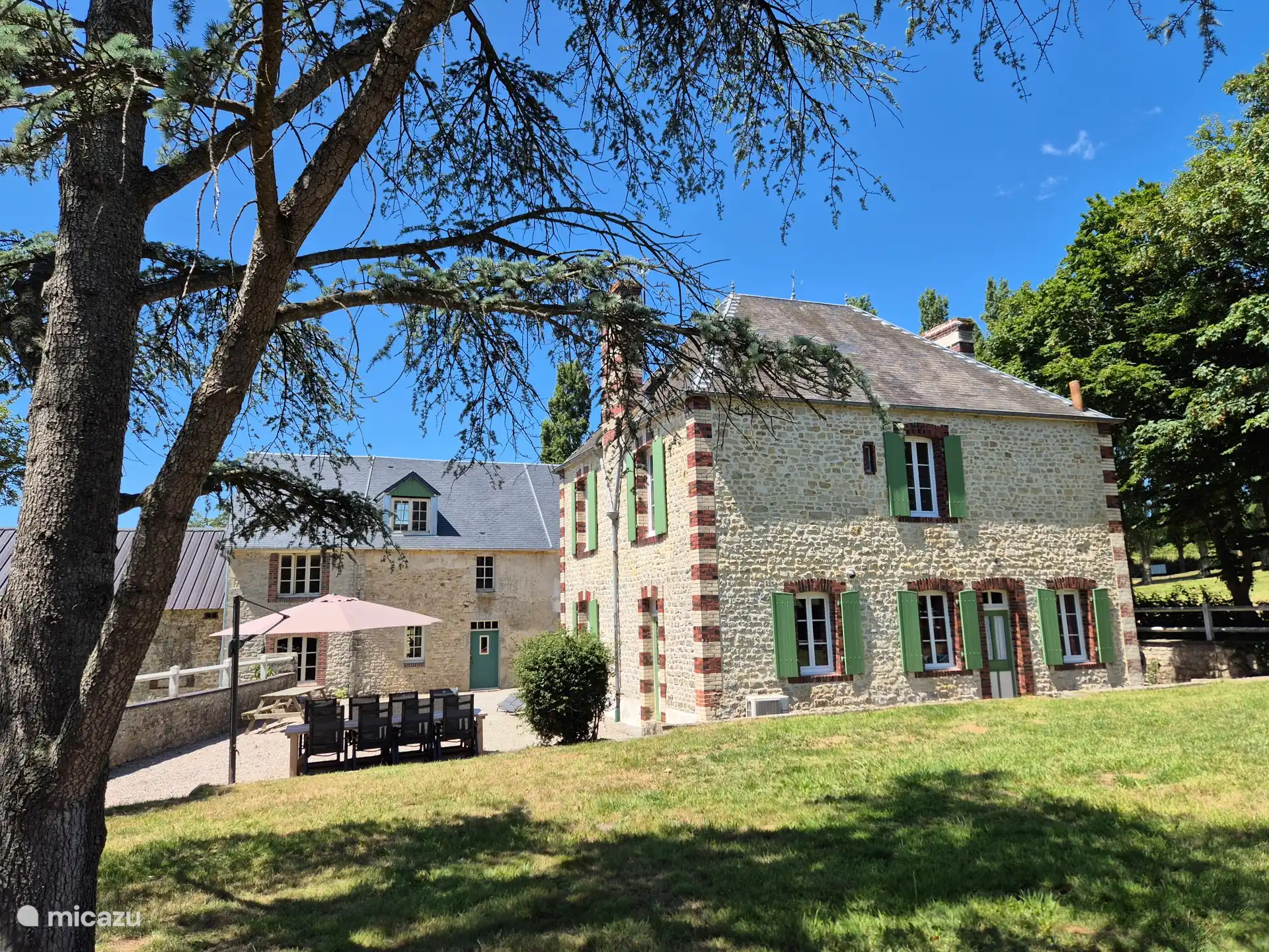 Schöner Garten rundum mit Gartenmöbeln, Picknicktisch, Sonnenschirm und zwei Sonnenliegen.