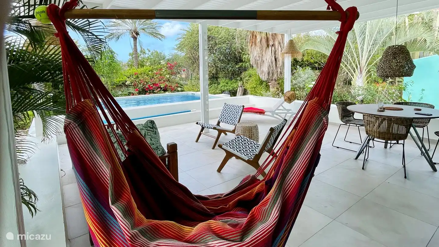 La véranda offre divers coins salons, un fauteuil suspendu et une chaise longue.