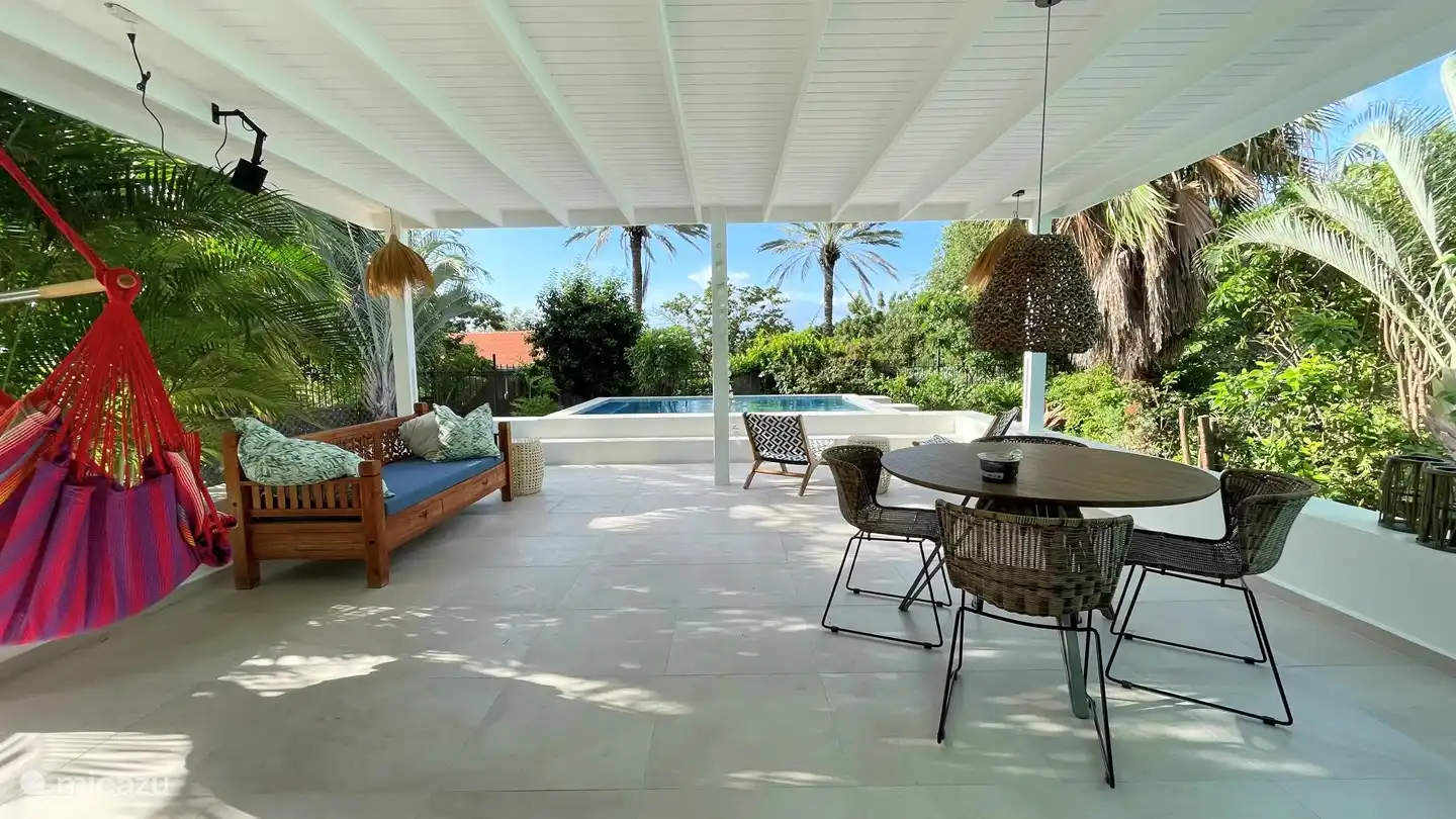 La spacieuse véranda couverte avec vue sur la piscine et le jardin tropical.