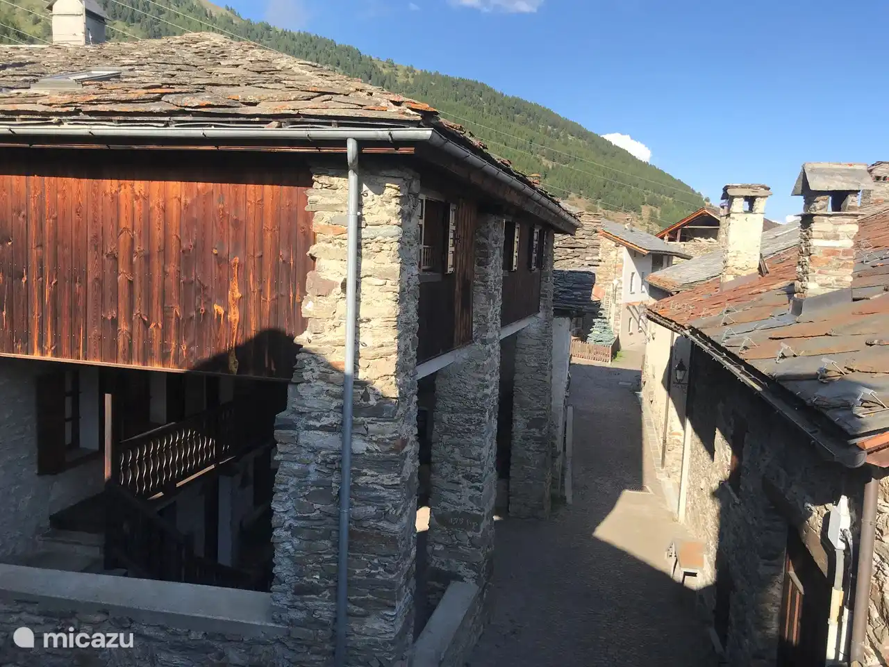 West-Süd-Fassade des Hauses. Wie die meisten Häuser im Dorf ist es aus Stein gebaut und verfügt in den oberen Etagen über Holzelemente. Der Holzbalkon ist mit einer wunderschönen geschnitzten Balustrade geschmückt.