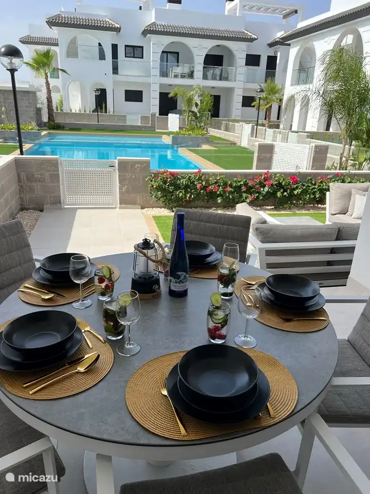 Esstisch im Freien auf der überdachten Terrasse mit 5 Esszimmerstühlen inklusive Kissen und Blick auf den Swimmingpool.