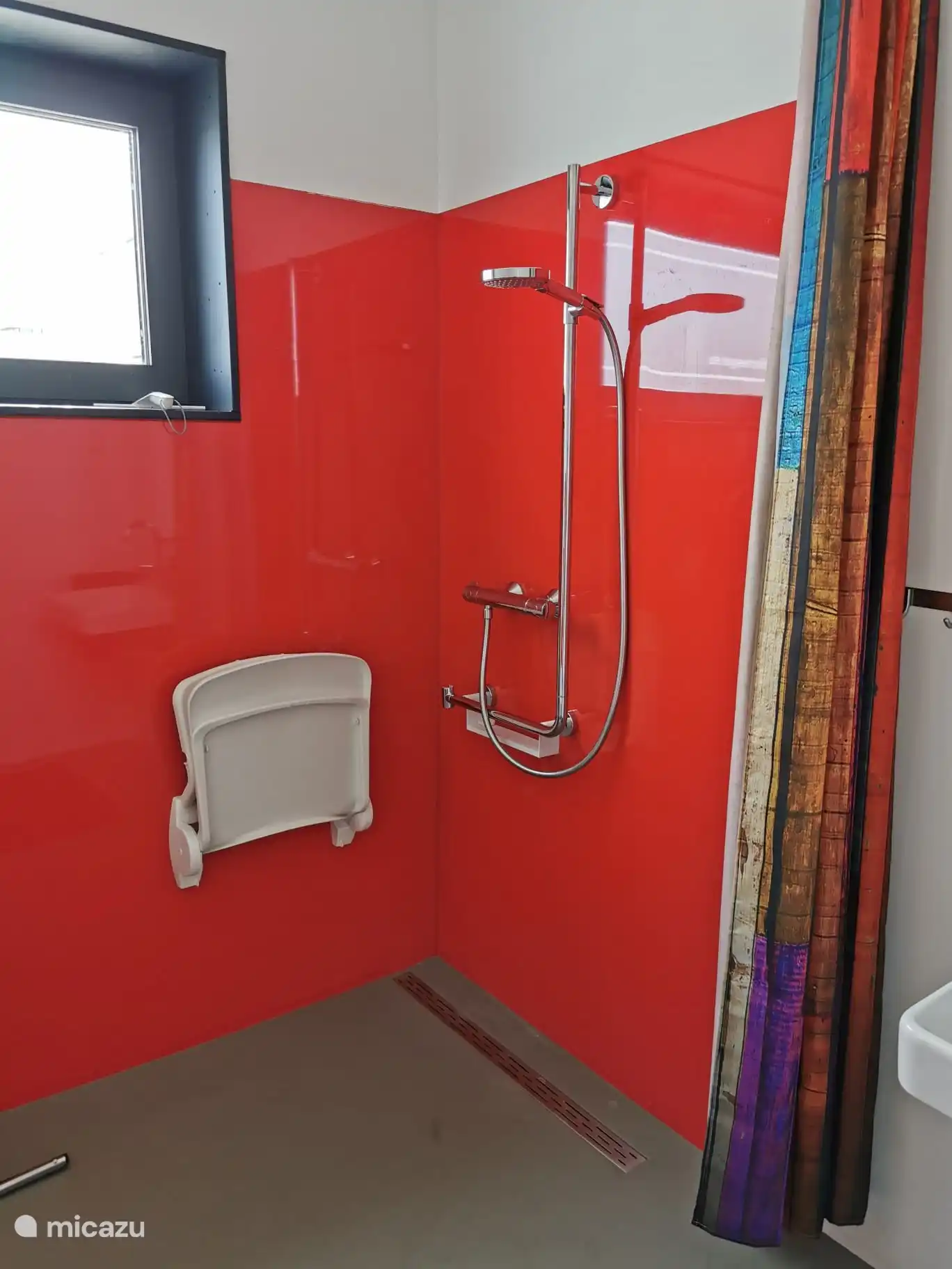 Ein großzügiger Raum zum Duschen, ausgestattet mit einem extra langen Handlauf und der Möglichkeit, sich beim Duschen hinzusetzen.