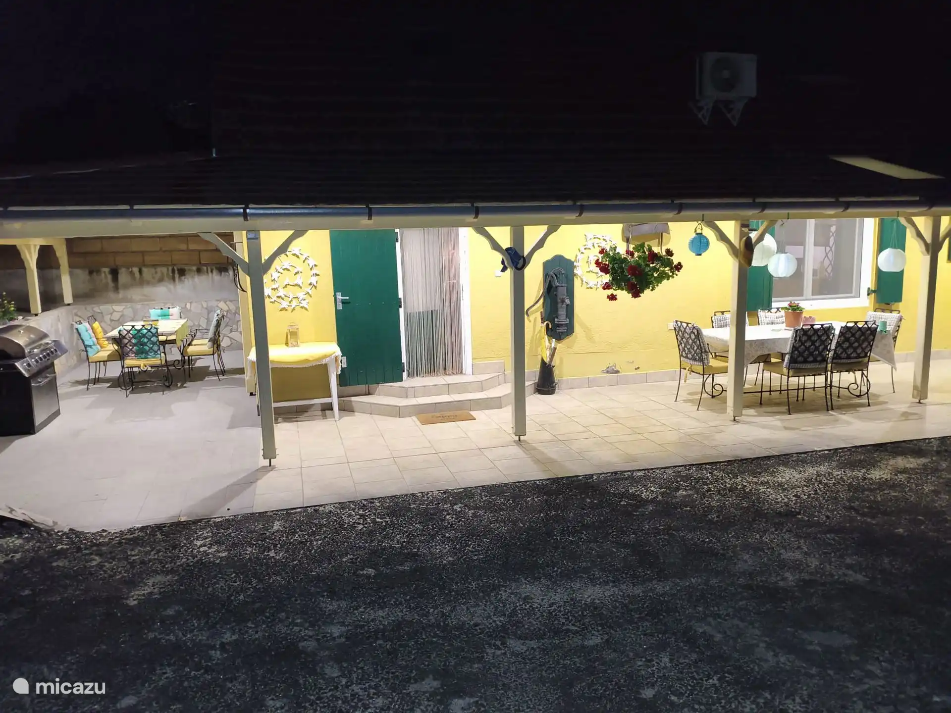 Vista de las dos terrazas de la casa de vacaciones con grandes mesas (de comedor) y barbacoa de gas.