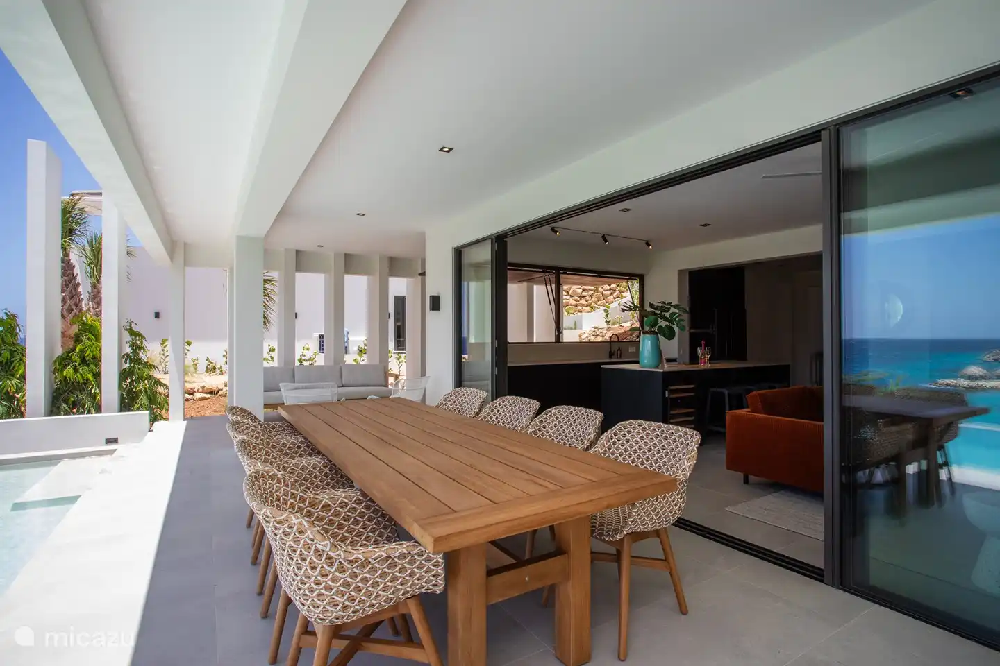 Spacieuse véranda ombragée avec entrée sur séjour et cuisine intérieure.