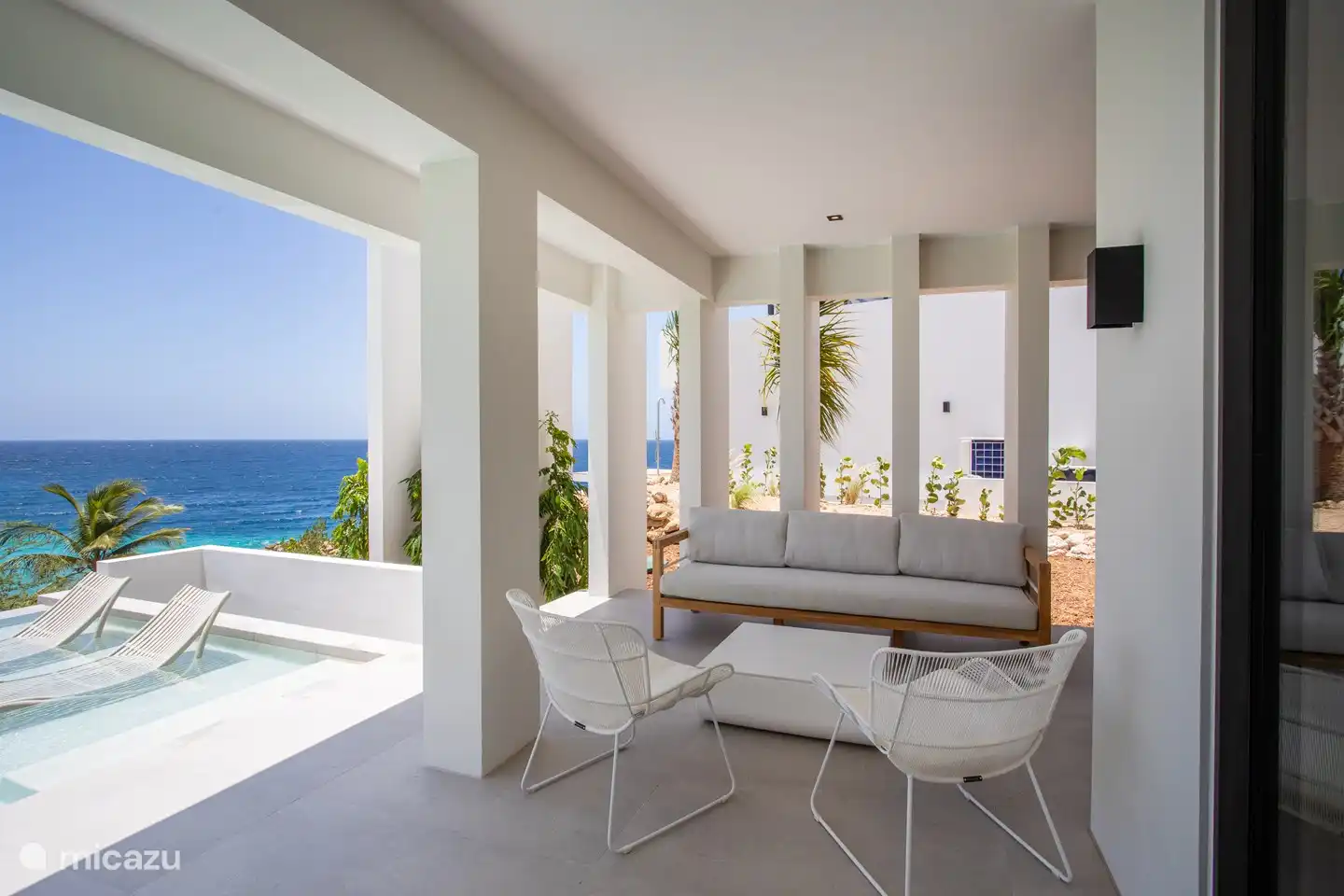 Spacieuse véranda ombragée avec coin salon, surplombant la baie de Blue Bay.