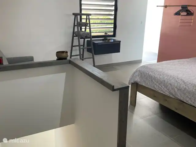 BohoGarden B - Fully airconditioned huren in Curaçao, Banda Ariba (oost), Jan Thiel - appartement Ruime slaap kamer met een hoge King size bed en een slaapbank met een open slaande deur naar het balkon waar je uitkijkt op het Binnenhof van Boho garden. Achter de wand bevind zich de douche.