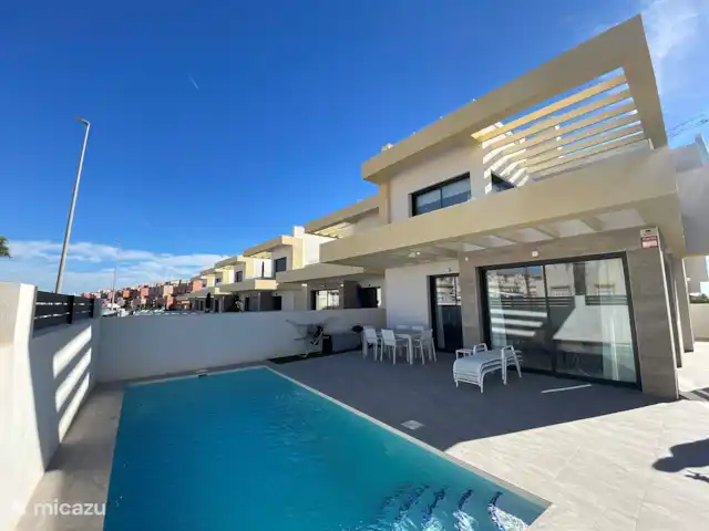 Villa Séréna | Espagne, Costa Blanca, Los Montesinos - villa Vue sur la villa, comprenant la piscine et la terrasse avec chaises longues et table à manger extérieure. La zone est accessible depuis la cuisine ainsi que le salon.