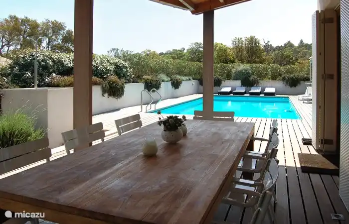 Under the porch at the large wooden table with 8 chairs you find a nice view on the terraces, garden and the pool