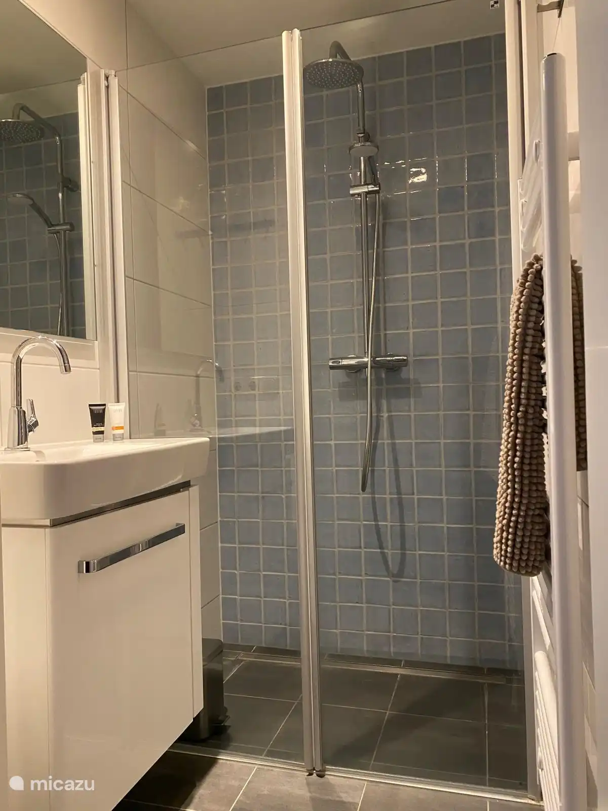 Salle de bain avec douche à effet pluie, serviette, radiateur sèche-serviettes et lavabo.