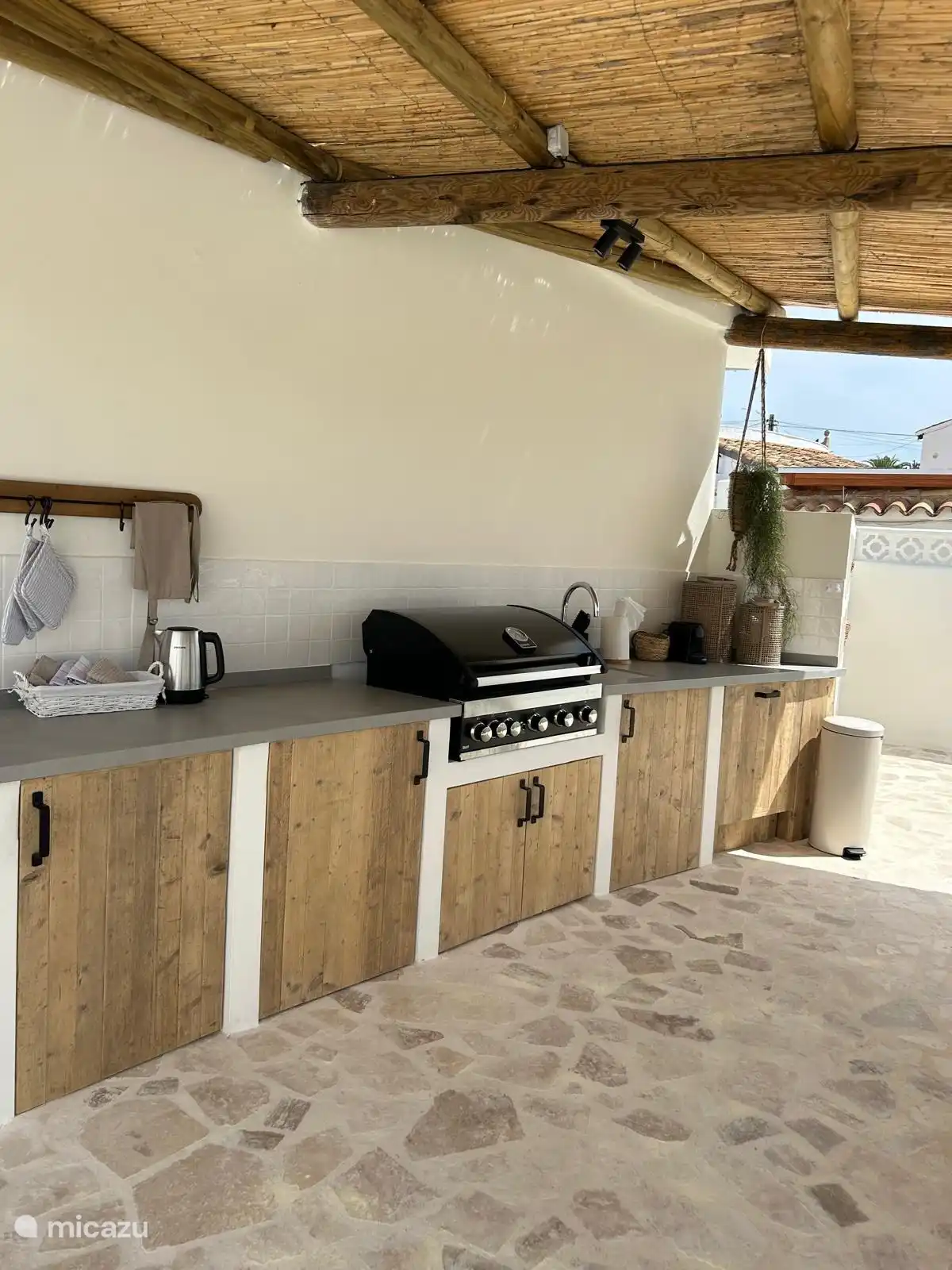 Pérgola Villa Laurel con generosos 8-pers. Área de comedor con mesa de tronco de árbol y cocina al aire libre con refrigerador, barbacoa de gas, lavaplatos.