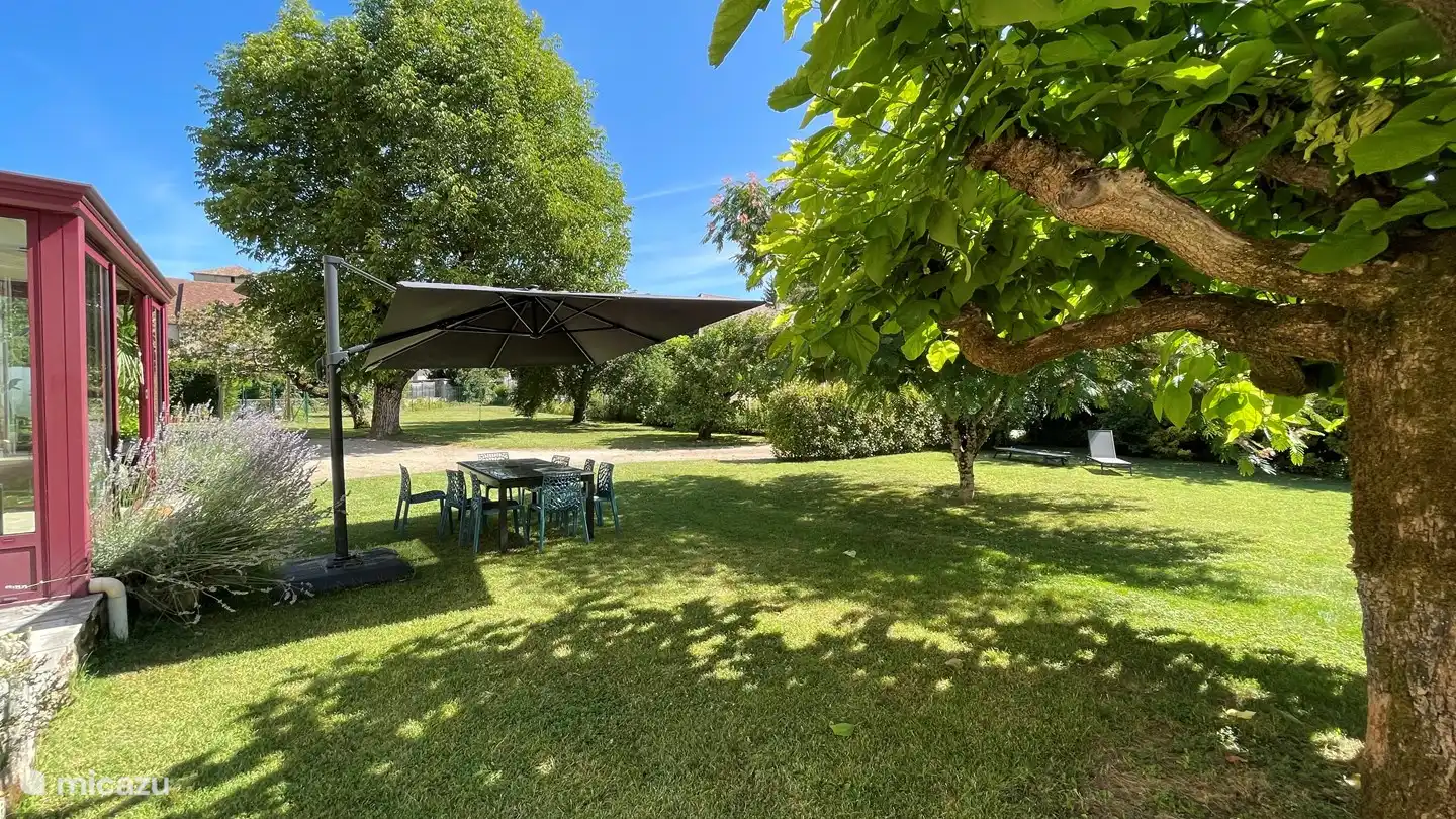 De volgroeide tuin heeft een grote tafel en een grote parasol