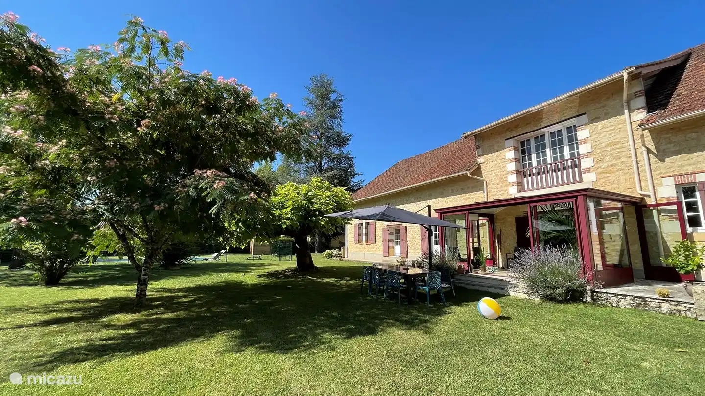 De volgroeide tuin heeft een grote tafel en een grote parasol