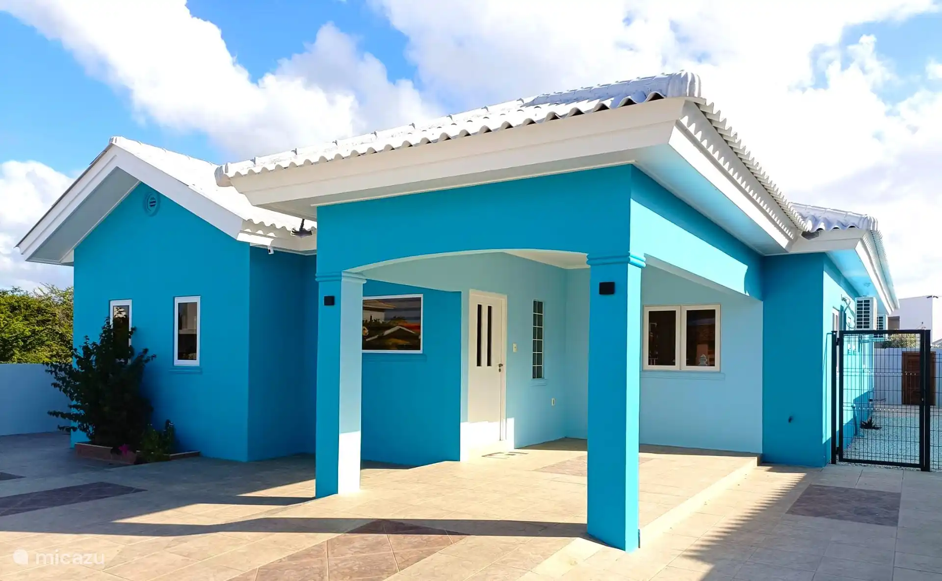 Front of the house. The front door is under the roof. The entire front has a tiled floor. The entire plot is fenced.