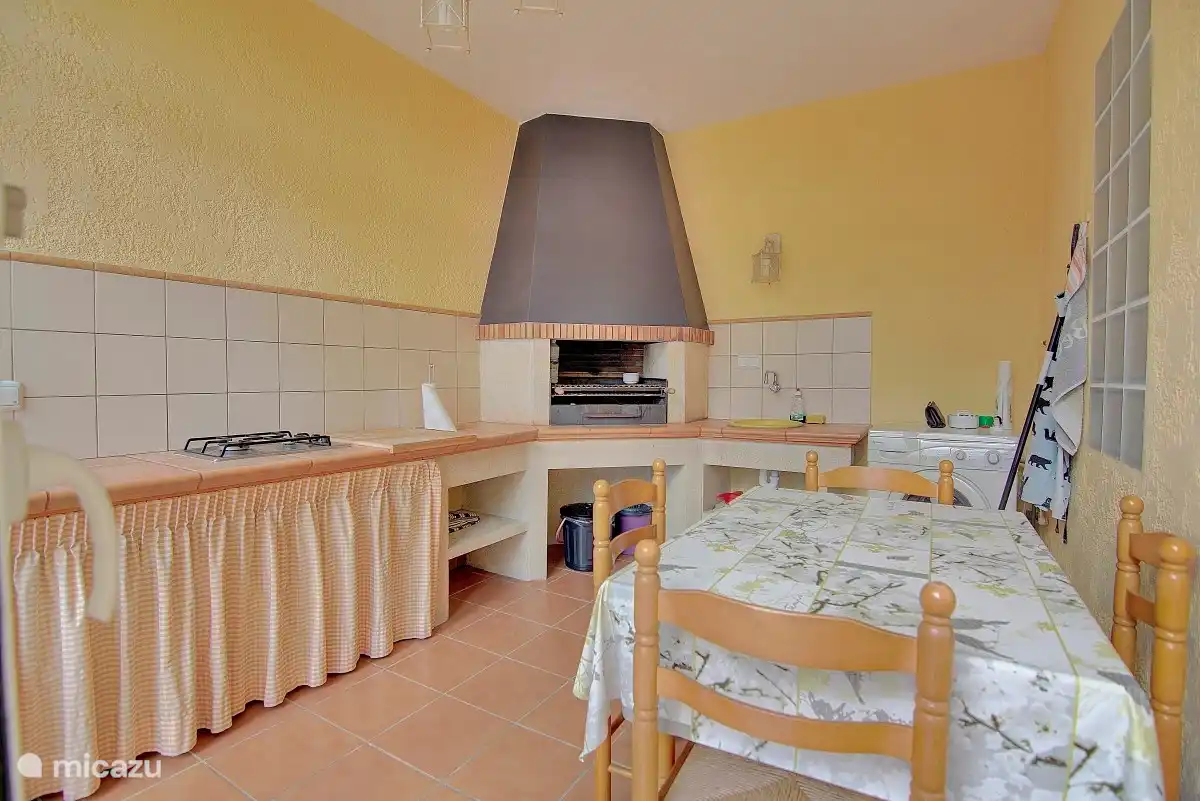 Il y a un barbecue avec une cuisine et un barbecue à bois à l'intérieur avec des pinces pour la nourriture et des ustensiles en fer pour le nettoyer. Poubelle et bouteille de butane pour la cuisinière à gaz. Il y a une table extensible avec quatre chaises. Banc pour travailler dans la cuisine.