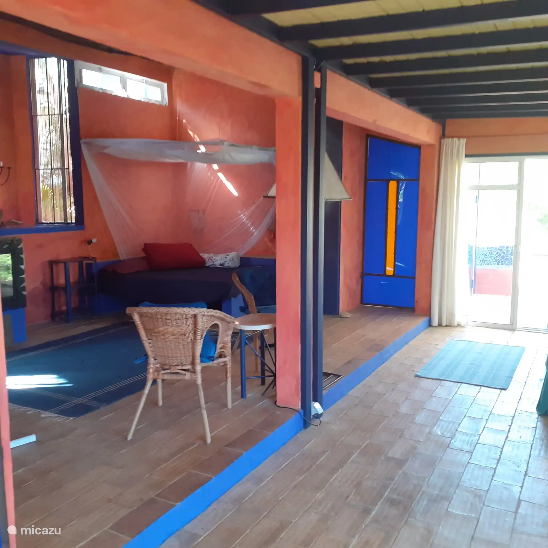 Eindruck des Lebensraums mit integriertem Doppelbett und Mueckenschutz und der blauen Eingangztuer zum Schlafzimmer.