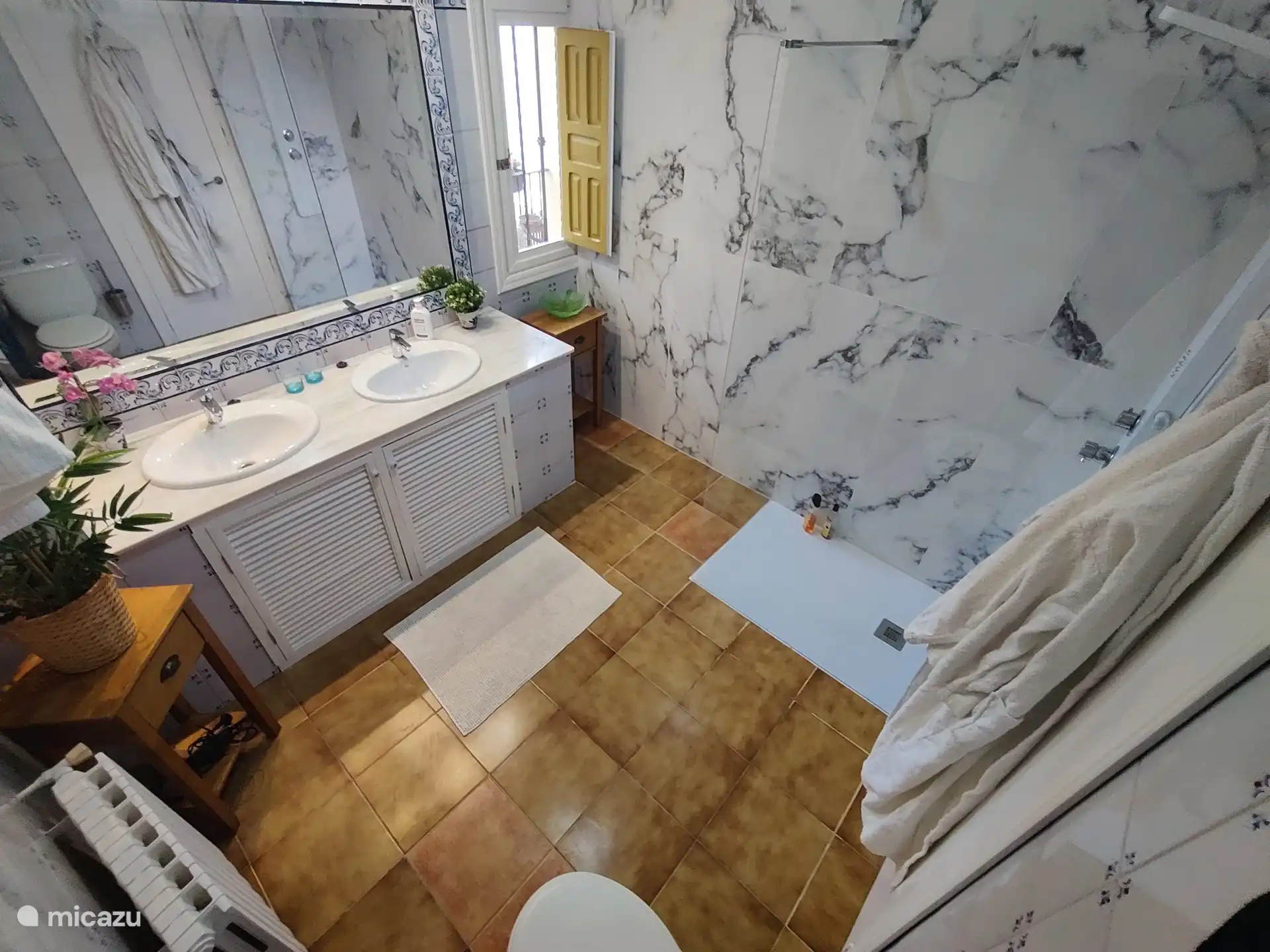 Amplio cuarto de baño con ducha a ras de suelo, doble lavabo e inodoro.