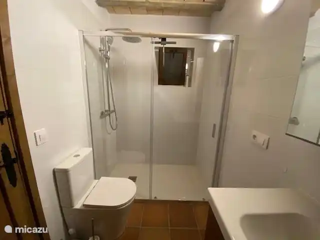 Salle de bain avec douche à effet pluie et régulière, meuble sous-vasque avec armoire à glace et sèche-cheveux. Toilettes avec couvercle à fermeture douce