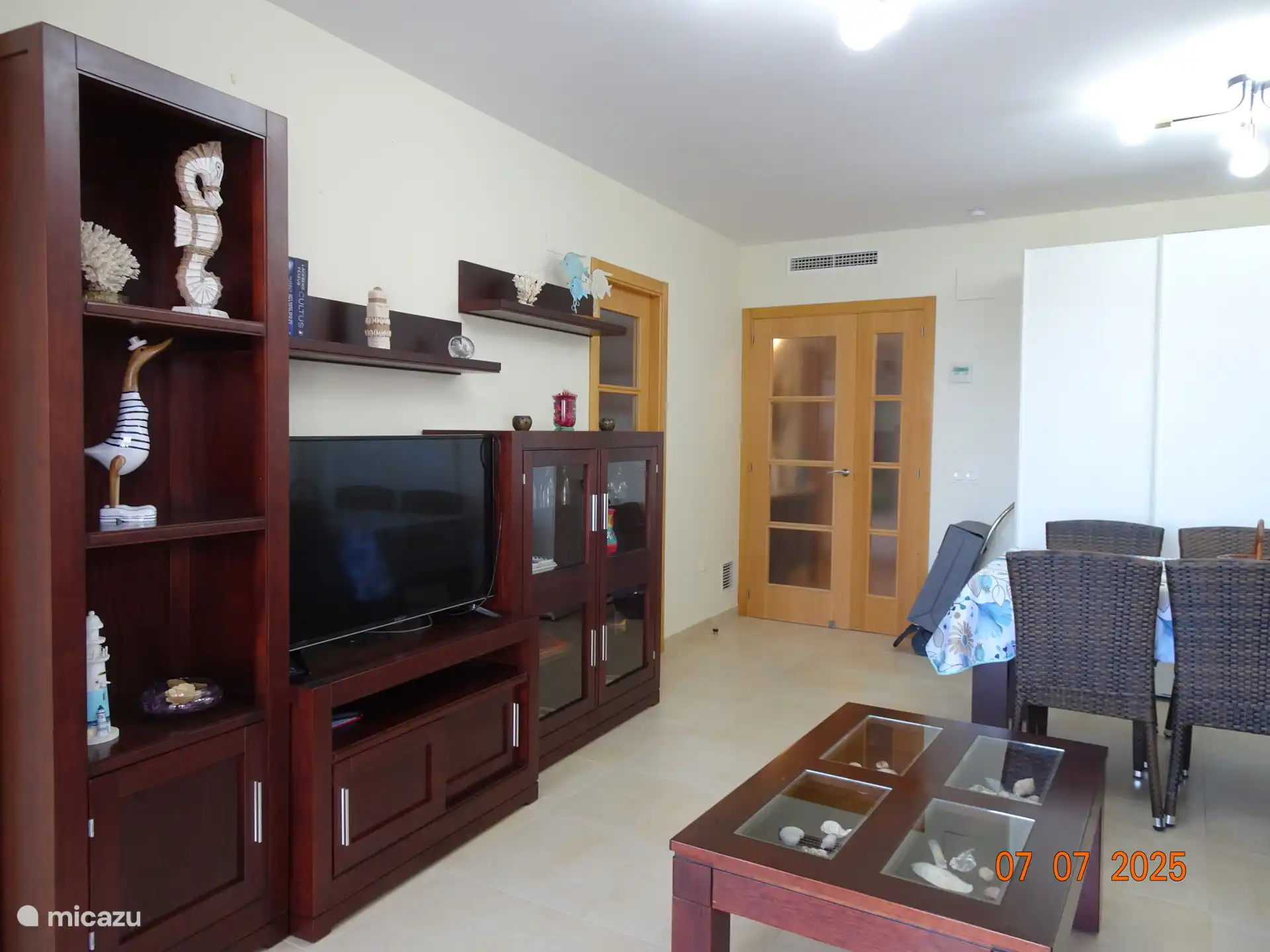 Wohn- / Esszimmer mit Zugang zur Küche und zum Eingangsbereich. Es gibt eine zentrale Klimaanlage/Heizung. Im Wohnzimmer befindet sich ein großer Fernseher