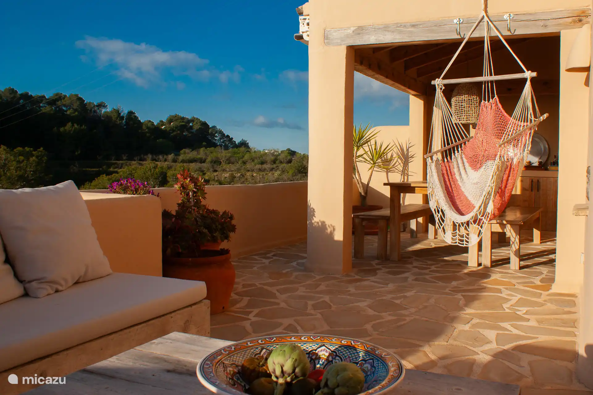 Overdekt terras op de begane grond met comfortabele zithoek met loungekussens en een schommelstoel.