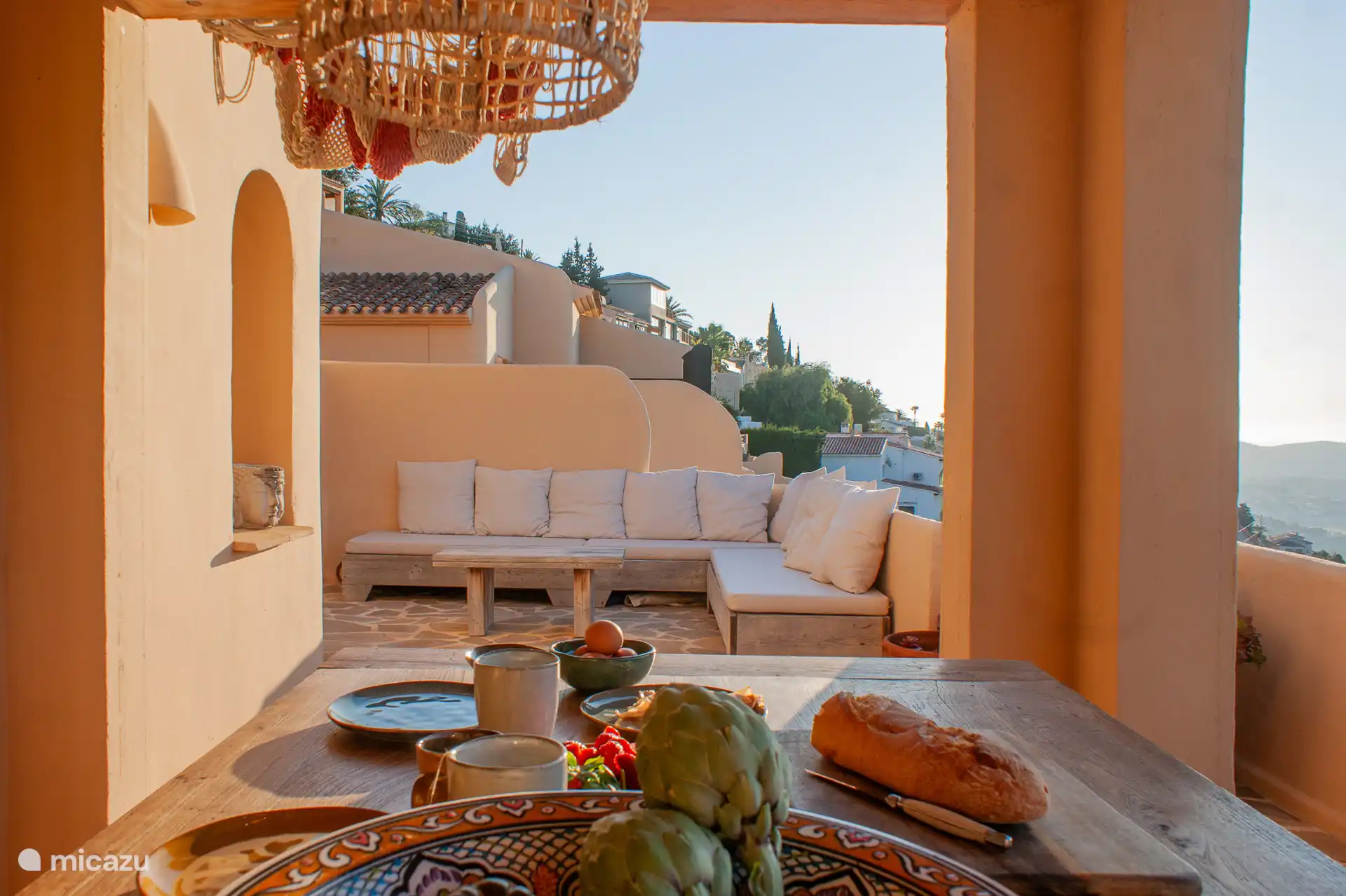 Overdekt terras op de begane grond met prachtig uitzicht, een ruime eettafel voor 6 personen, een comfortabele zithoek met loungekussens en een buitenkeuken.