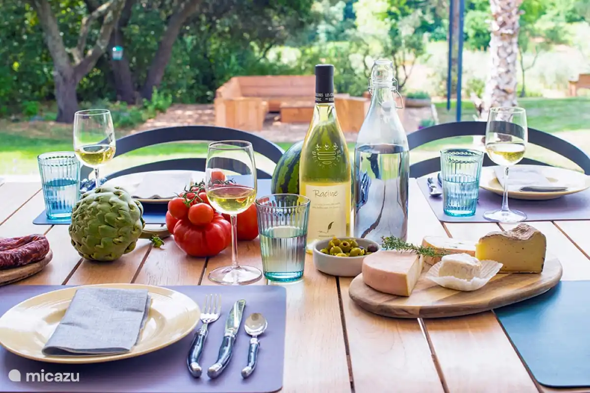 Gedeckter Esstisch mit Blick auf die Loungegarnitur, das Tal und den Weinberg