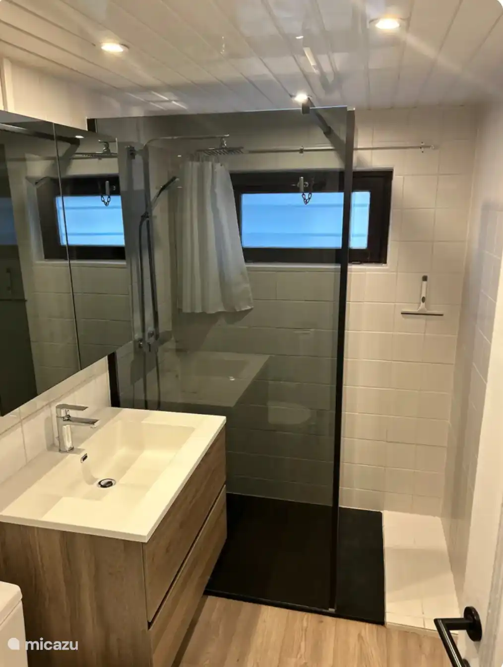 Baño reformado con cabina de ducha, lavabo e inodoro.