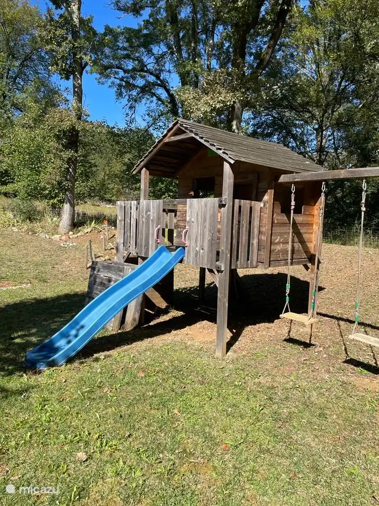 Kinderspielhaus mit Schaukeln und Klettergeräten direkt neben der überdachten Außenküche.