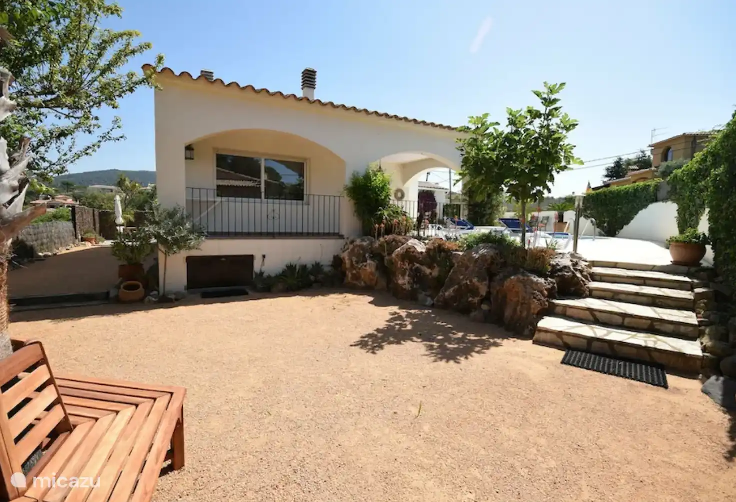 Seitlich am Haus mit einer Baumbank rund um die Palme.