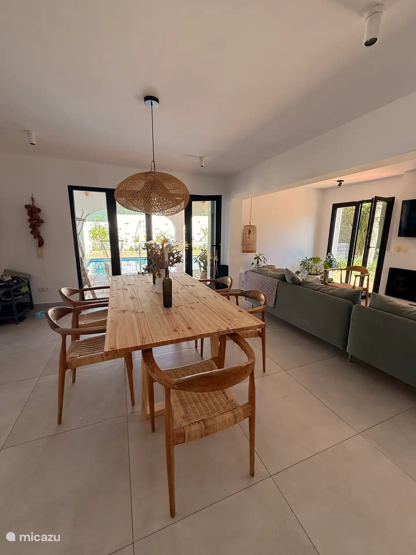 Großer Essbereich neben offener Küche, Wohnzimmer und Eingangsterrasse mit Blick auf den Garten und den Pool.  