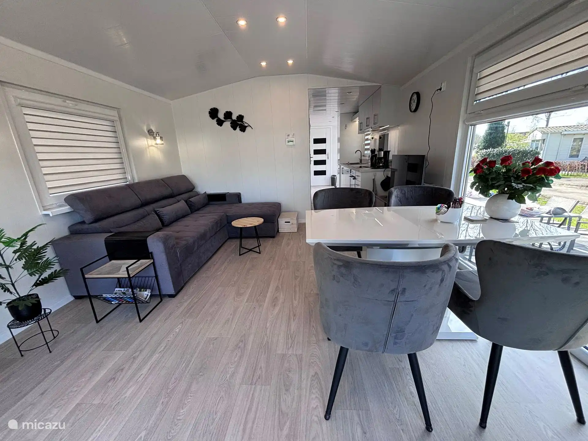 Sala de estar con cocina contigua y comedor frente a un gran ventanal con vistas al camping.