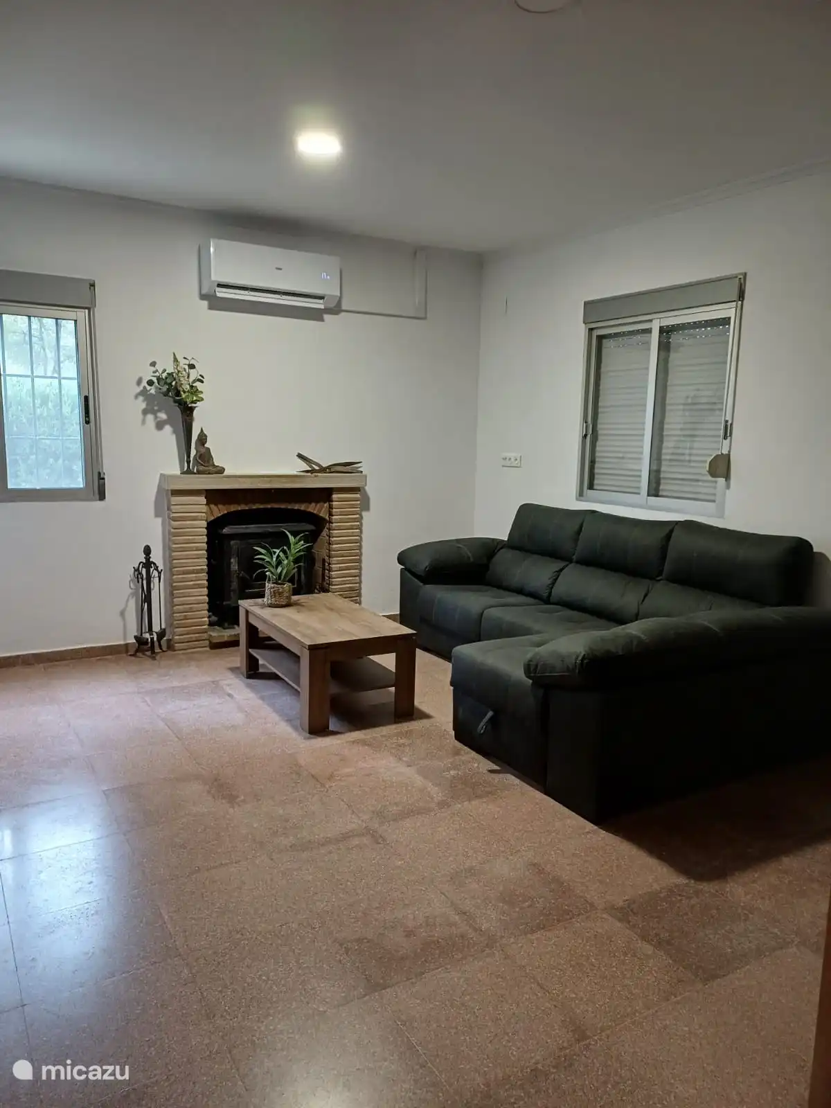 Der schöne Sitzbereich. Hier sind der Holzofen aus Speckstein und das Ecksofa zu sehen. Rollladen ist geschlossen, kann aber geöffnet werden. Fenster hinter dem Sofa gibt den Blick auf den Wintergarten frei, der mit den Türen verschlossen ist.