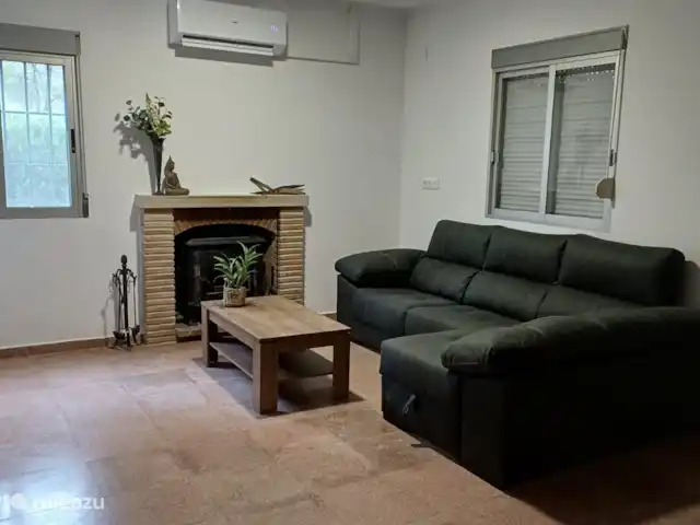 Villa Morera en España, Valencia, Albaida - villa La preciosa zona de estar. Aquí se puede ver la estufa de leña de esteatita y el sofá esquinero. La persiana está cerrada pero se puede abrir. La ventana detrás del sofá ofrece una vista del invernadero que está cerrado con las puertas.