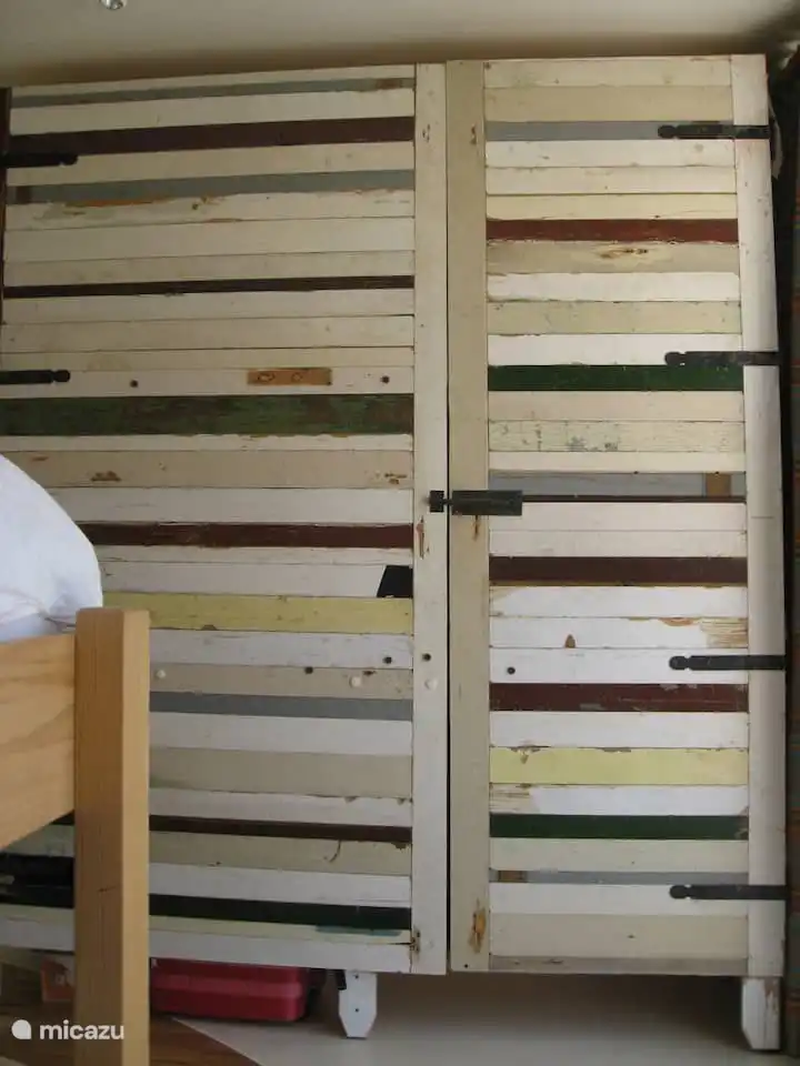 Großer Gerüstholzschrank im Zimmer mit drei Betten. Platz für Kleidung auf Kleiderbügeln und in Regalen.