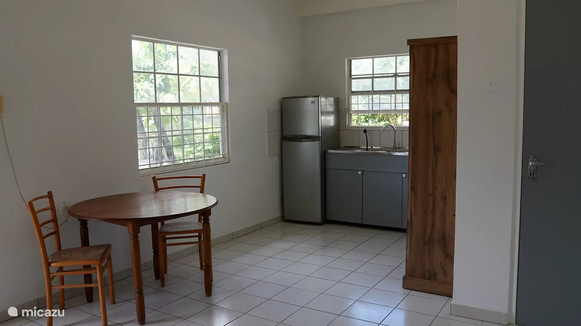 Küche mit Kühlschrank, Gefrierschrank, Herd, Backofen, Wasserkocher, Klimaanlage, Ventilator und Kühlbox sowie Esstisch für zwei Personen