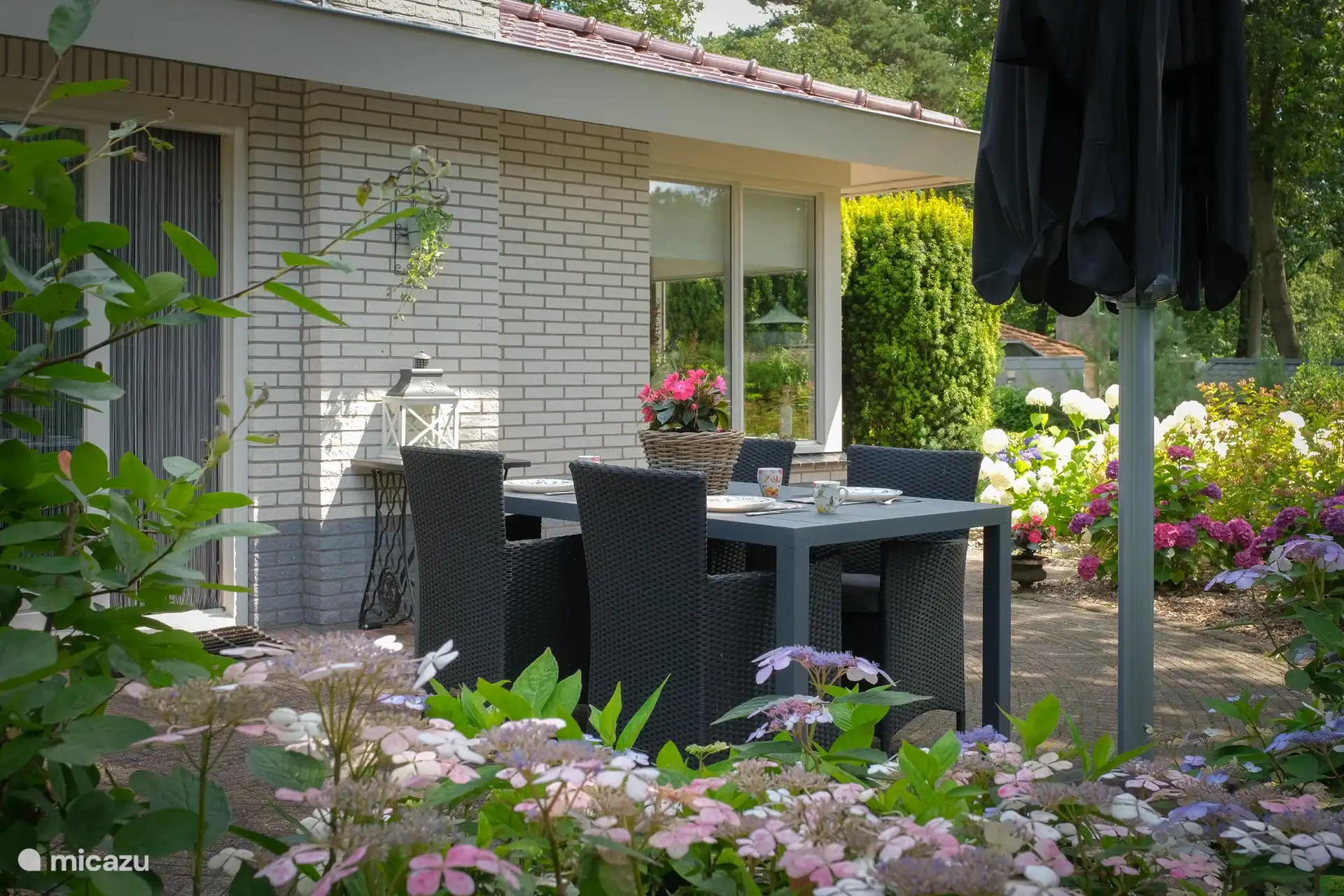 Terrasse mit großzügigem (Wald-)Garten mit vielen blühenden Pflanzen, Bäumen und Sträuchern