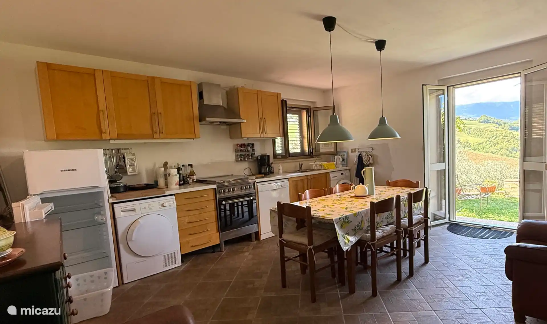 Amplia cocina con lavadora, secadora y lavavajillas, frigorífico-congelador alto y puertas que dan a la terraza orientada al oeste.