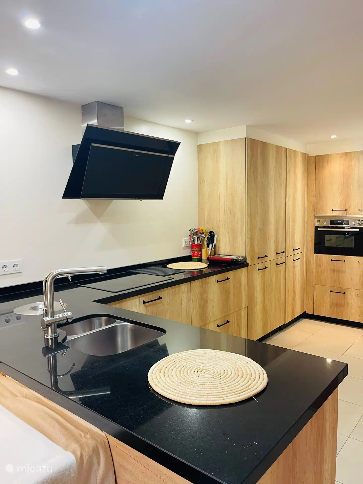 Nouvelle cuisine avec plateau en pierre, réfrigérateur-congélateur, four mixte, lave-vaisselle, divers placards avec vaisselle et appareils de cuisine.