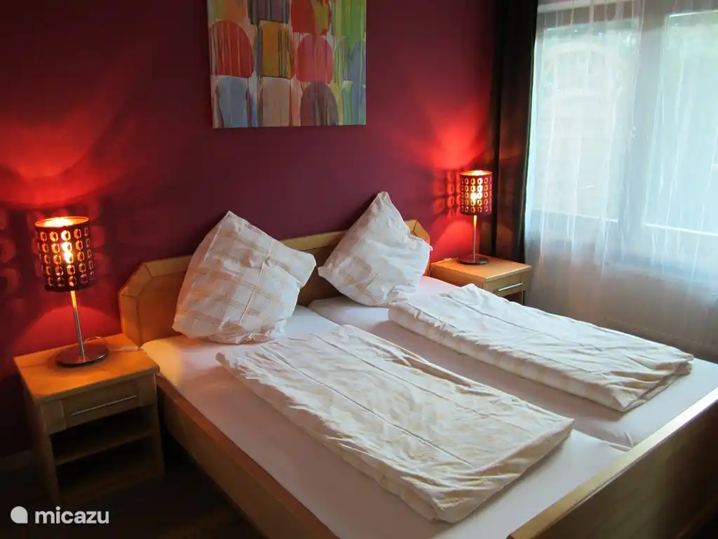 Das geräumige Schlafzimmer mit rotem Doppelbett mit einem gemachten Bett von 180 cm Breite und 200 cm. 