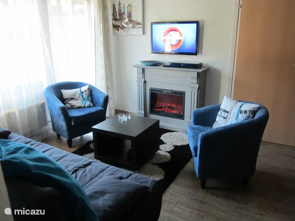 Gemütliches Wohnzimmer mit dekorativem Kamin, großem TV-Bildschirm von 104 cm, (Schlaf-)Sofa und 2 bequemen Sesseln. 