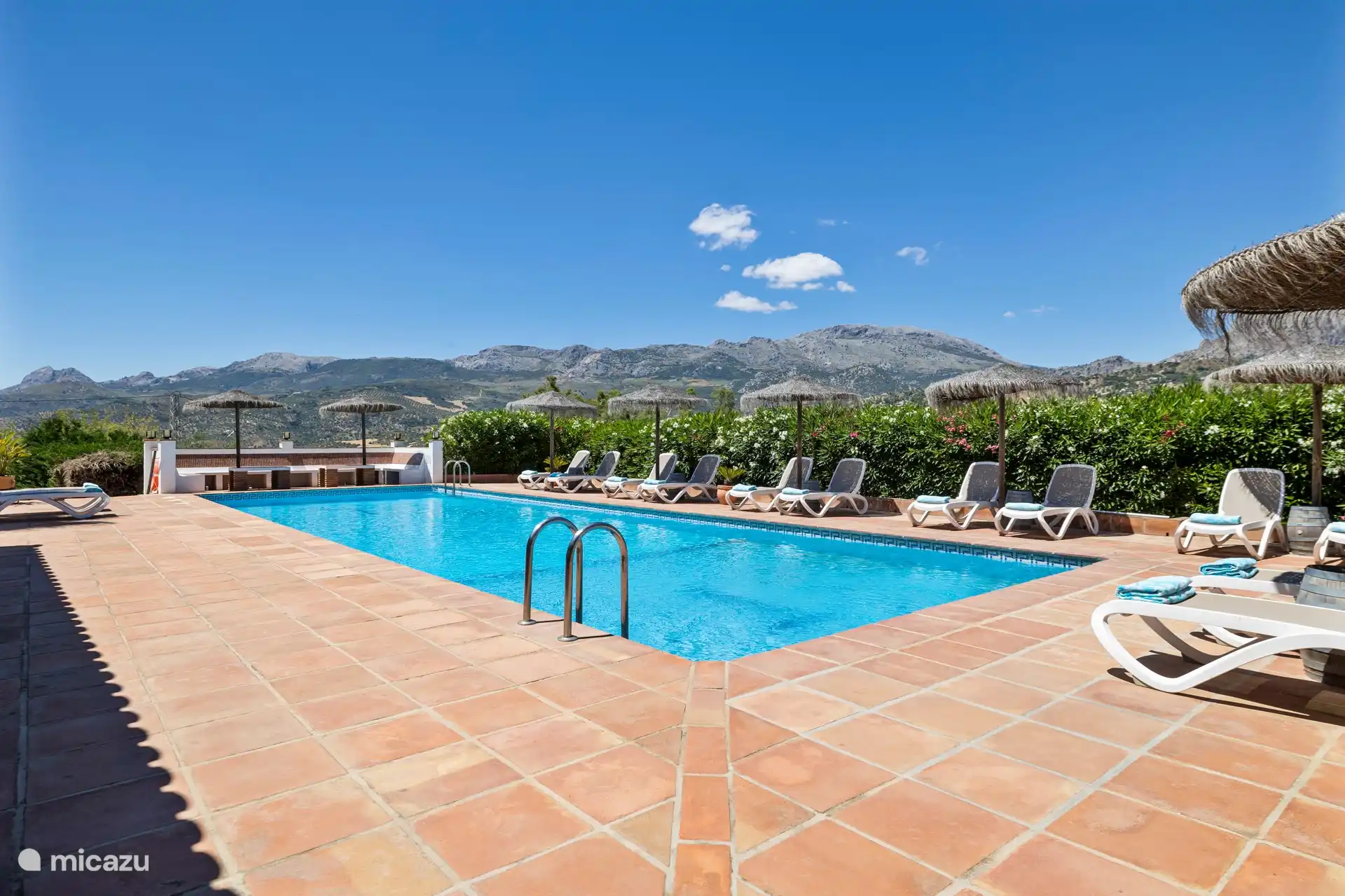 La amplia piscina con sombrillas y tumbonas