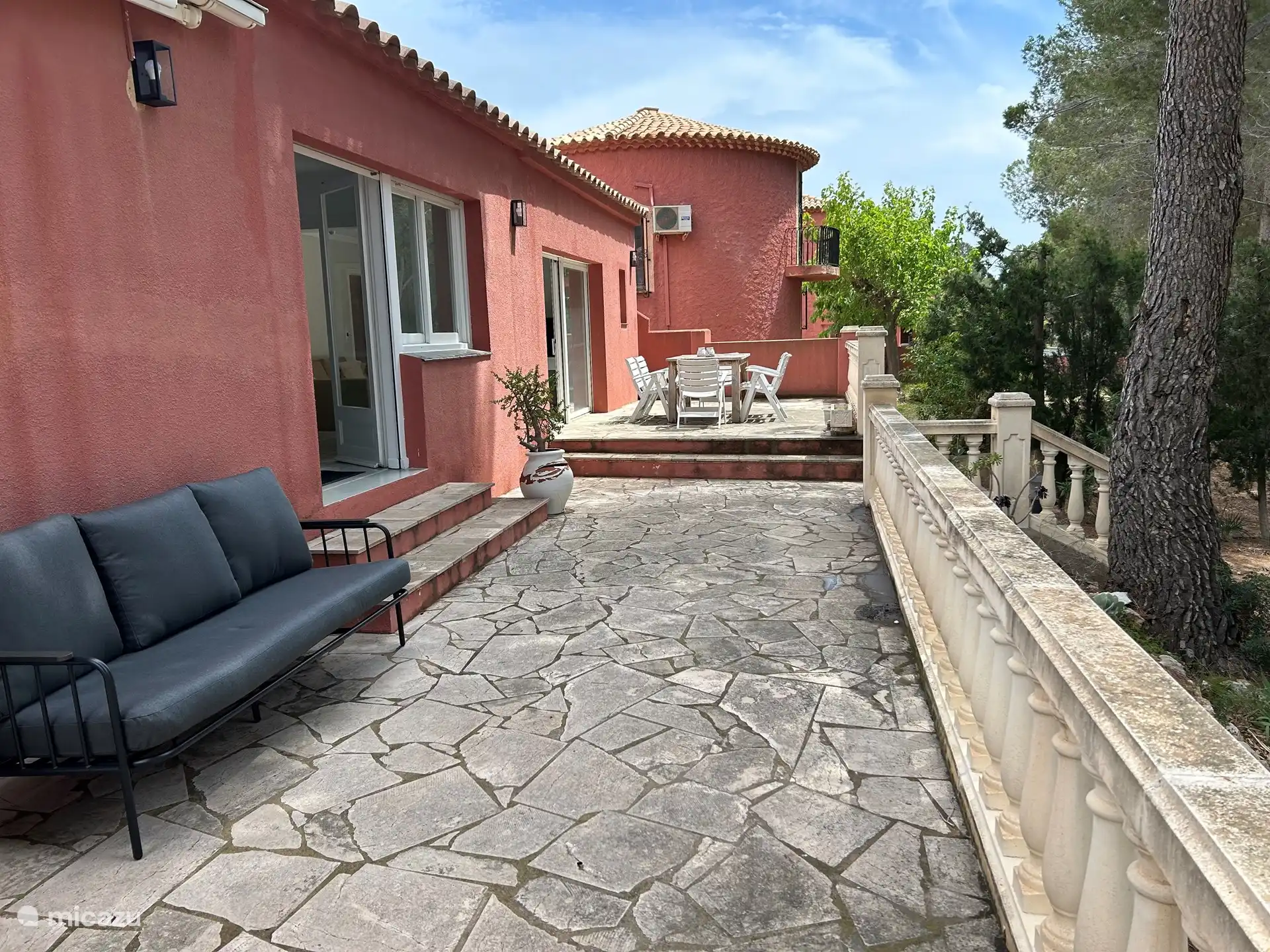 Het terras met een tuinbank en zitje en een tafel met stoelen met kussens, een barbecue 