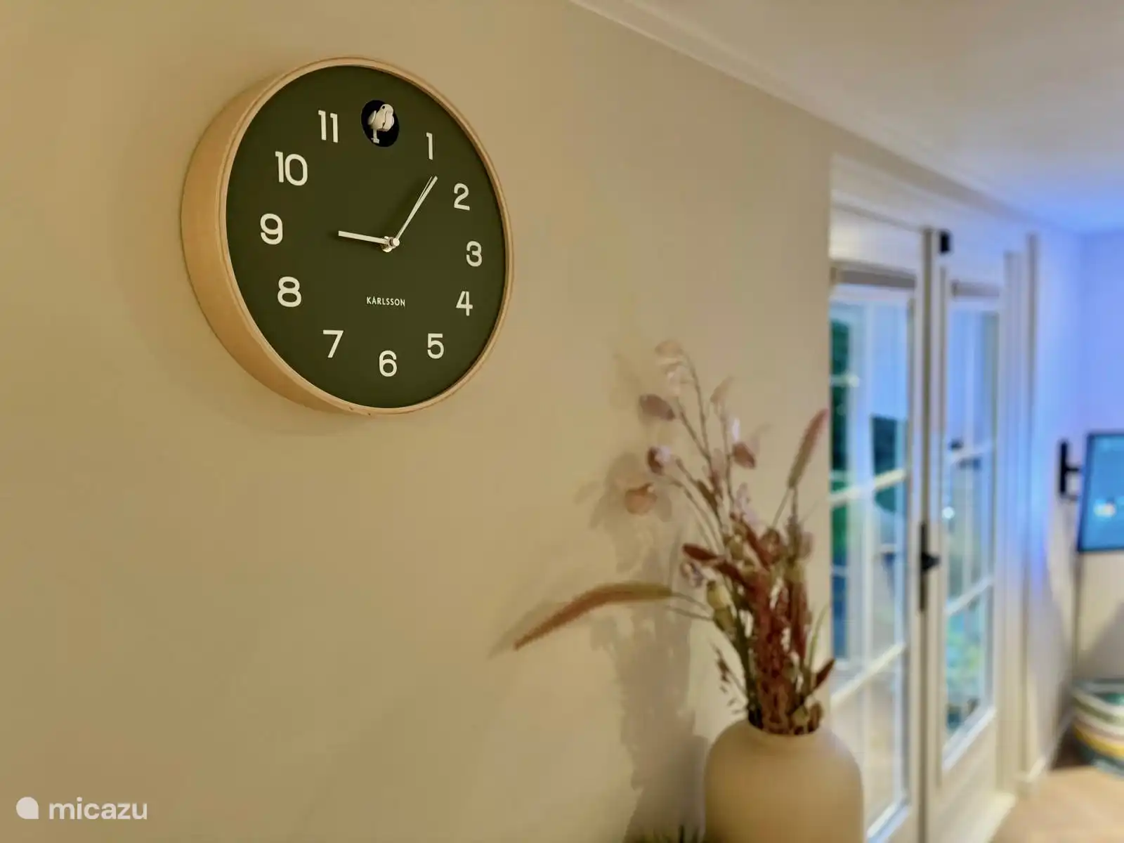 
Die ruhige Wand im Wohnzimmer strahlt Schlichtheit und Gelassenheit aus, mit einer modernen Kuckucksuhr als stilvolles Detail. Die Uhr passt perfekt zum natürlichen Thema des Hauses und verleiht der entspannten Atmosphäre eine verspielte, zeitgemäße Note.