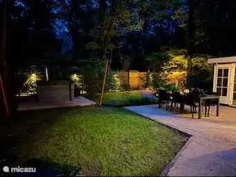 Der Garten strahlt am Abend eine magische Atmosphäre mit sanfter Beleuchtung aus, die das Grün und die Details wunderschön zur Geltung bringt. Die Terrasse lädt zu einem entspannten Abend unter dem Sternenhimmel ein, während das warme Licht der Lampen ein gemütliches und ruhiges Ambiente schafft.