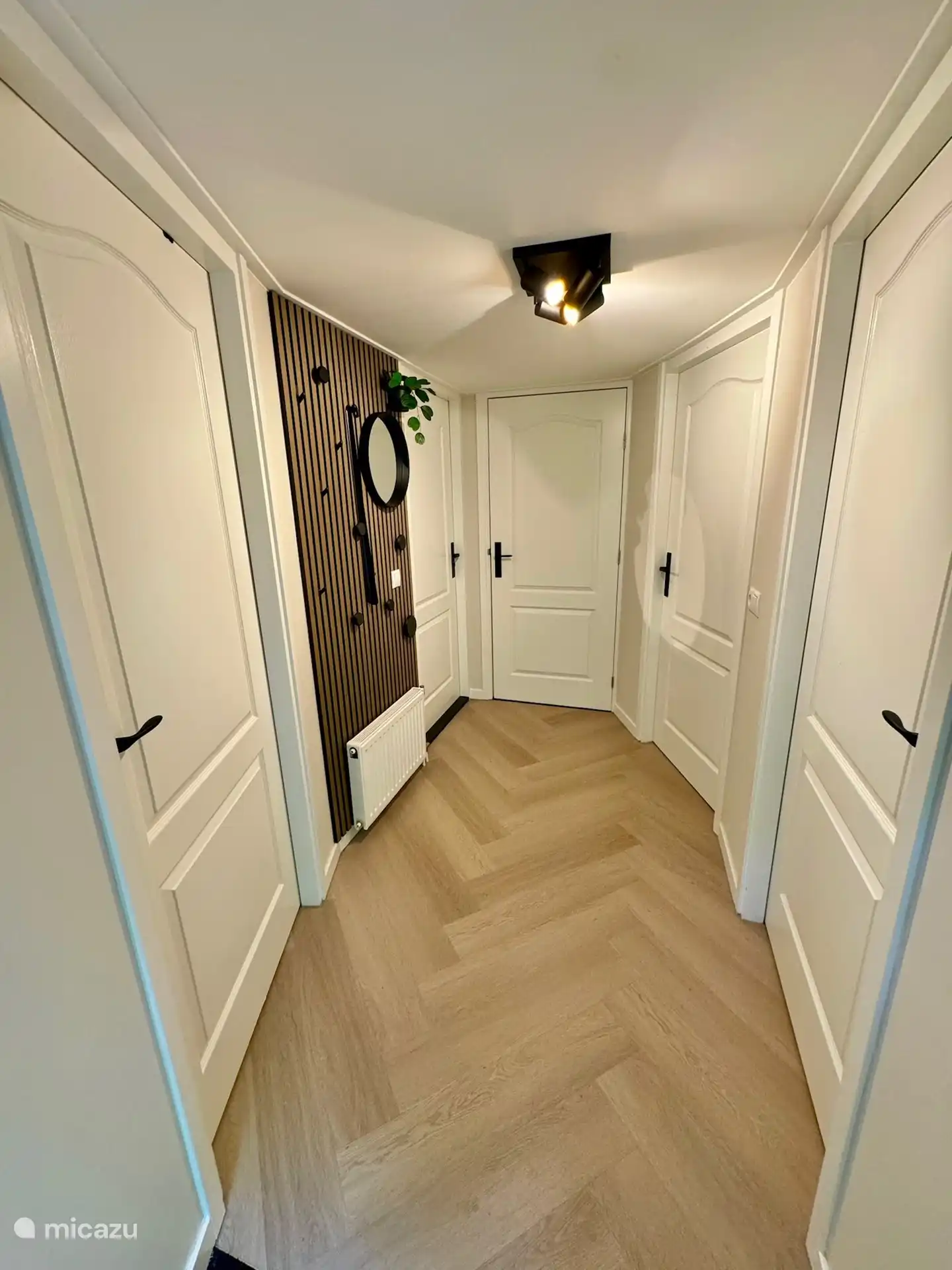 
Beim Betreten befinden Sie sich in der zentralen Halle, die attraktiv mit einer Garderobe aus PET-Filz, einer warmen Eichenlattenwand mit schwarzen Knöpfen und stilvollen Accessoires eingerichtet ist. Ein Spiegel und eine grüne Pflanze vervollständigen das Ganze. Der schlanke, frische Look schafft sofort ein herzliches Willkommen und ein Gefühl von Zuhause.