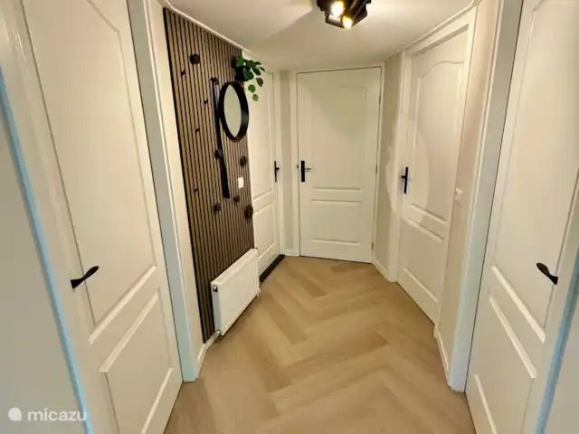 Maison de vacances Maridu Family Wellness | Pays-Bas, Gueldre, Hattemerbroek - chalet 
Dès l’entrée, vous êtes dans le hall central, joliment décoré avec un porte-manteau en feutre PET, un mur en lattes de chêne chaleureux avec des boutons noirs et des accessoires élégants. Un miroir et une plante verte le complètent. Le look élégant et frais crée immédiatement un accueil chaleureux et un sentiment de maison.