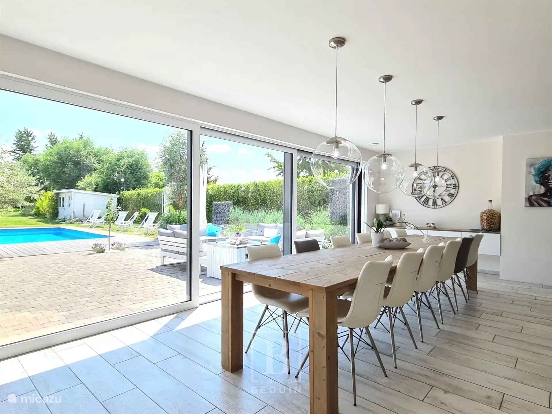 Gran mesa de comedor en salón abierto de 105m². Andamio de mesa de madera para 14 personas. Grandes ventanas correderas para obtener la máxima luz. Vista a terrazas, jardín y piscina climatizada.