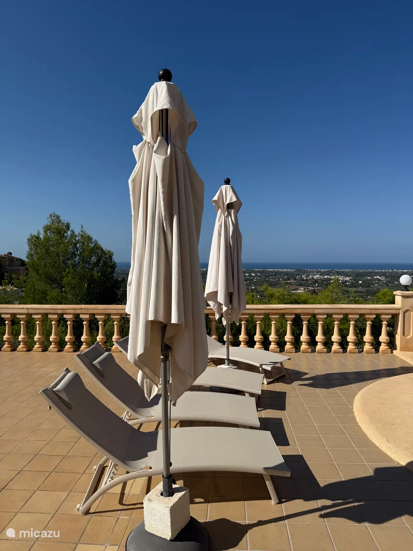 Terraza de la piscina con tumbonas y sombrillas y vistas al mar