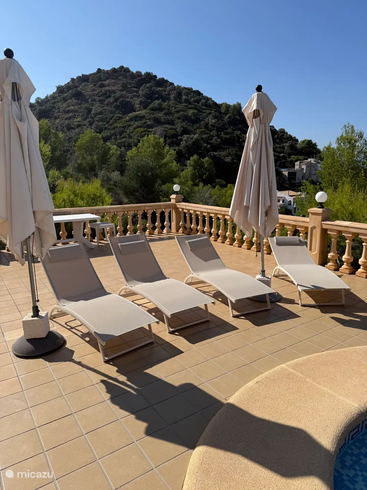 Terraza de la piscina con tumbonas y sombrillas con vistas al mar y a la montaña