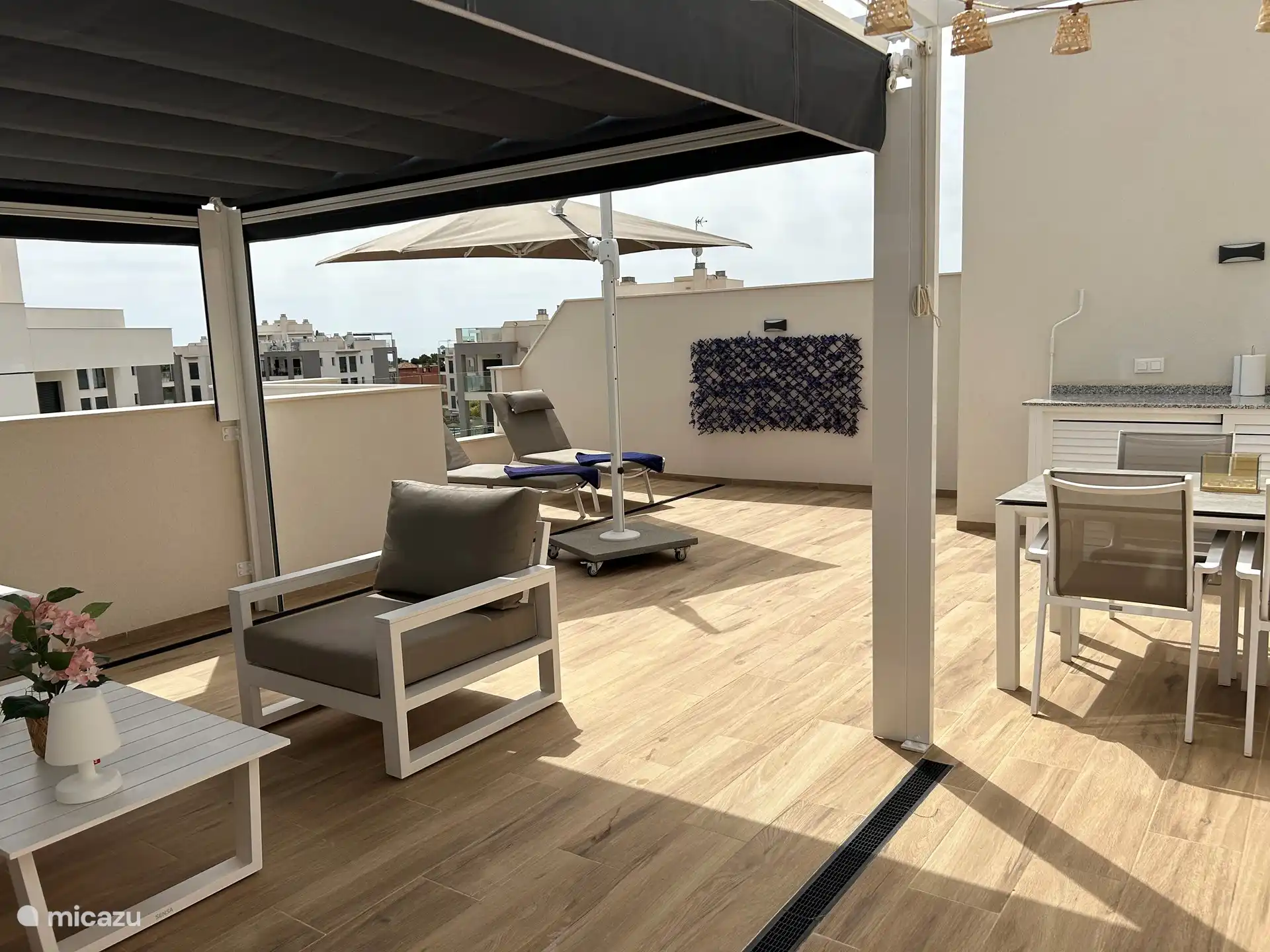 dakterras met ligstoelen en parasol en eettafel
